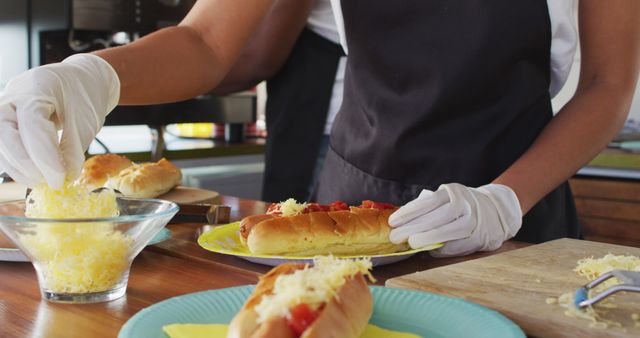 Chef professionally preparing delicious hot dogs with grated cheese in a modern kitchen. Ideal for use in food blogs, culinary magazines, recipe websites, promotional materials for cooking classes, and advertising gourmet fast food products.