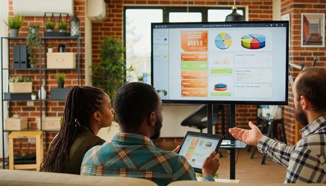Team reviewing interactive data dashboards on tablet and monitor in modern workspace