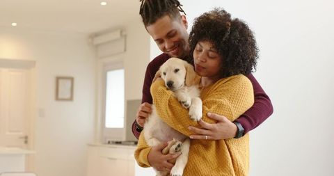 Young couple cuddling labrador puppy in bright cozy kitchen sharing warm affectionate moment