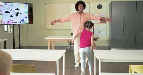 African American teacher welcoming excited young student into classroom with open arms