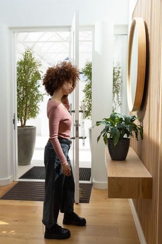 African american woman standing in modern minimalist entryway looking into round mirror