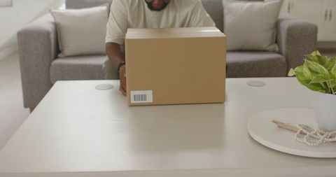 African man placing cardboard delivery box on coffee table in minimalist living room