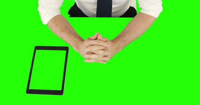 Businessman with hands clasped sitting at a desk, with tablet on green screen background. Useful for business presentation, corporate advertisement, and technology-themed projects.