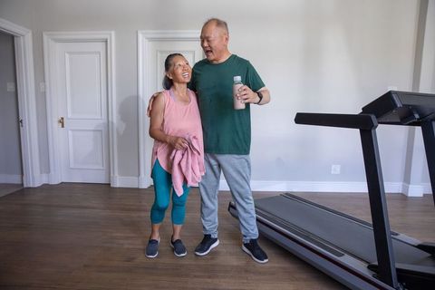 Senior couple celebrating post-workout by treadmill, smiling, hydrating and embracing