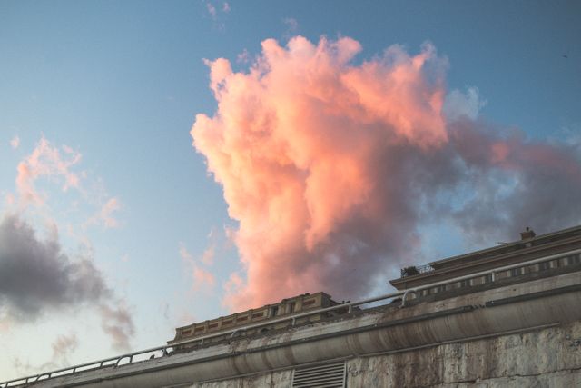 Vibrant orange cloud glowing in the evening light over an urban building. Could be used for illustrating contrasts between nature and urban environments, romantic dusk scenes, or atmospheric backdrops in blogs and magazines.