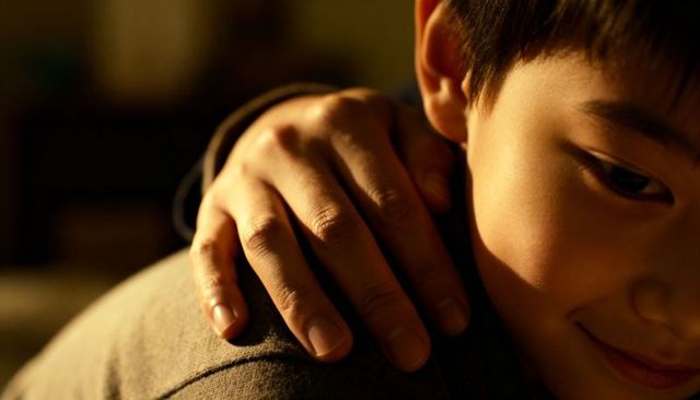 Gentle hand resting on child shoulder conveying warmth, trust and quiet family intimacy
