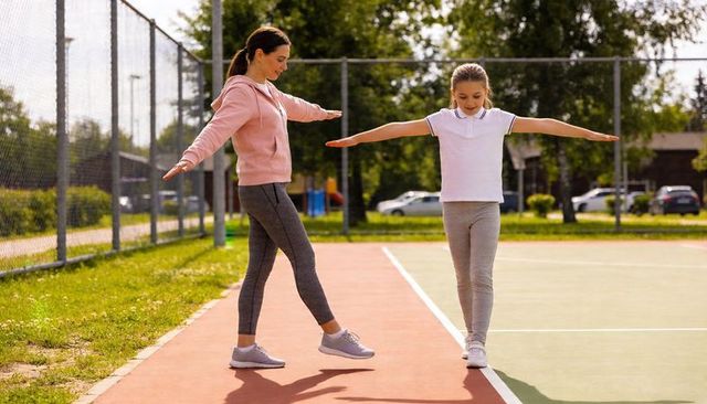 Parent and child practicing balance on court line in sunny community park