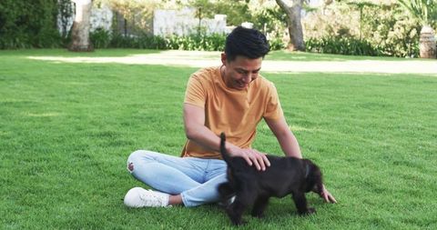 Young Man Relaxing with Cute Puppy on Sunny Lawn