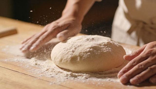 Shaping artisan bread dough with flour-dusted hands on rustic wooden work surface for bakery craft