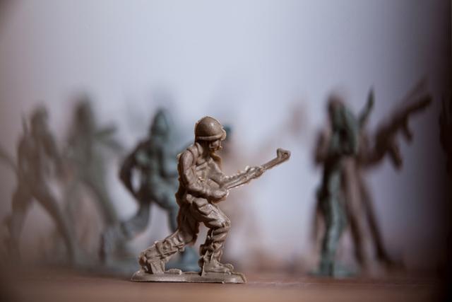 Miniature army soldier figurine depicted in a battle scene with other toy soldiers in the background. Ideal for use in articles or advertisements related to military history, toy collections, strategic games, or childhood play. Can also be used in educational materials about military tactics and history.
