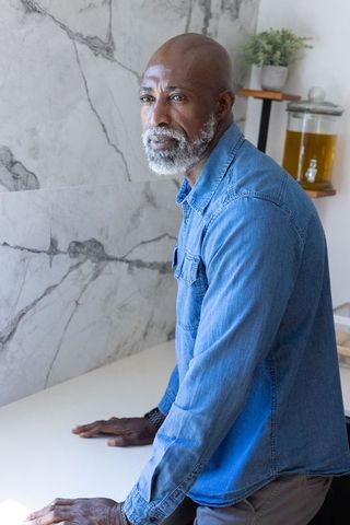 Contemplative african man leaning on white counter in modern kitchen with marble wall