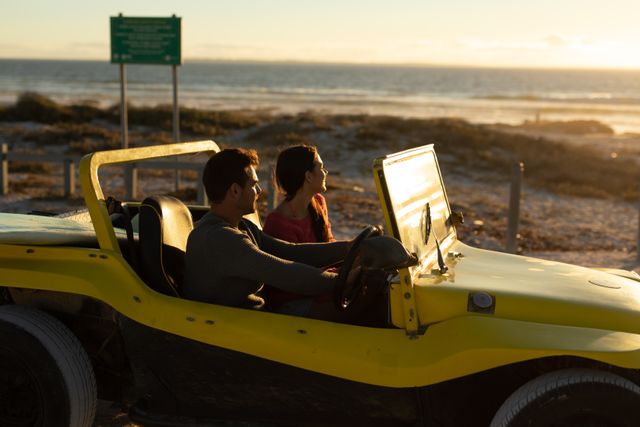 Couple driving a yellow beach buggy along the coastline at sunset, enjoying a romantic moment. Ideal for travel blogs, vacation advertisements, romantic getaway promotions, and lifestyle magazines focusing on adventure and leisure.
