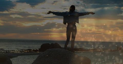 Woman Embracing Sunset on Rocky Coast with Glow