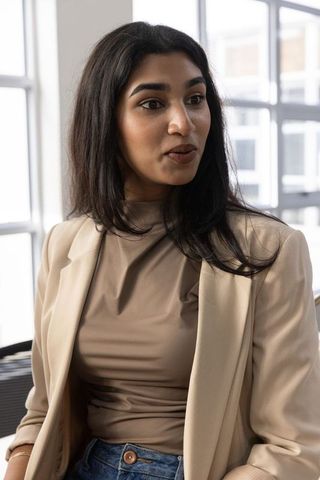 Indian woman working in bright modern office wearing beige blazer taupe top and jeans