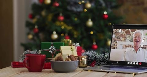 Senior woman video chatting on laptop during cozy christmas holiday with cookies and gifts