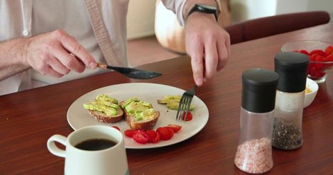 Man preparing avocado toast with tomatoes at home kitchen table