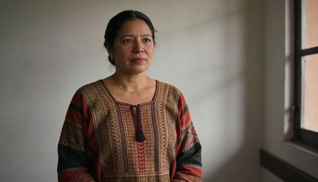 Calm woman standing near sunlit window wearing handwoven embroidered blouse with tassel
