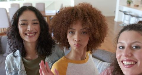 Diverse friends taking selfie on sofa in bright open-plan living room natural light