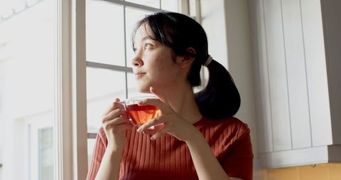 Asian Woman Relaxing with Cup of Tea by Kitchen Window