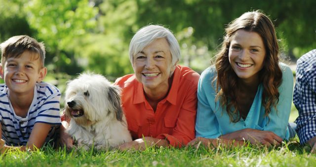 Three generations of a happy family, including a senior woman, young adults, and a child, smiling and enjoying peaceful time on a grassy field with their pet dog. Can be used for advertisements focusing on family, bonding, outdoor activities, and pet companionship. Also suitable for representing intergenerational relationships and healthy, active lifestyle content.