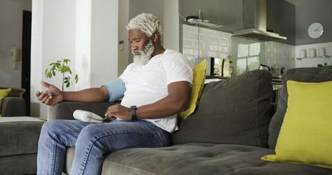 Senior man using blood pressure monitor at home on sofa