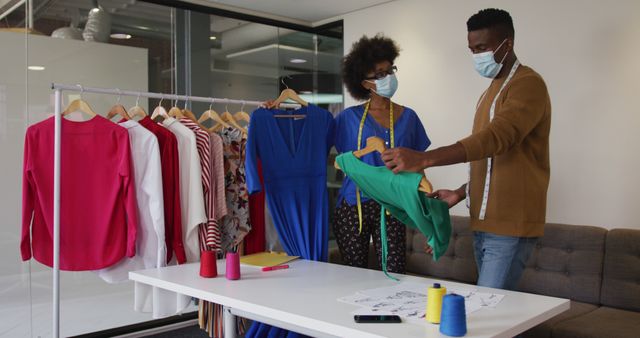 African american male and female fashion designers wearing face masks in discussion at work. independent creative design business during covid 19 coronavirus pandemic.