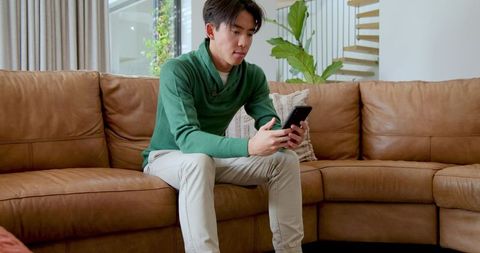 Man Relaxing with Smartphone on Modern Leather Sofa at Home