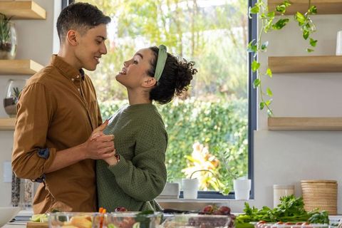 Young couple holding hands and cooking together in sunlit modern kitchen
