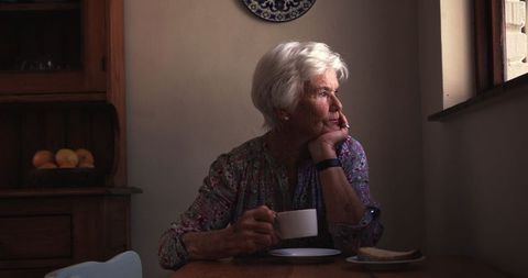 Elderly Woman Drinking Coffee While Reflecting By Kitchen Window