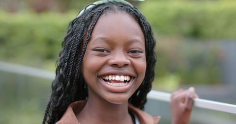 Radiant african american girl smiling with braided hair near metal railing, candid portrait