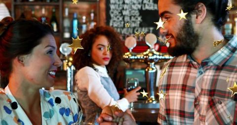 Fist-bumping friends at bar with bartender watching, smiling over wine, lively pub atmosphere