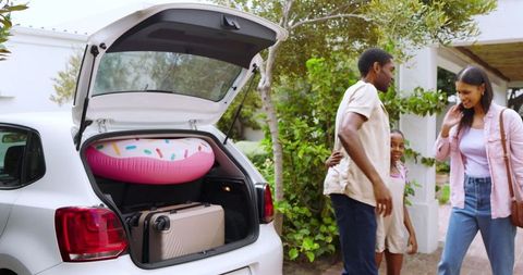 Family unloading luggage and inflatable float from car for vacation