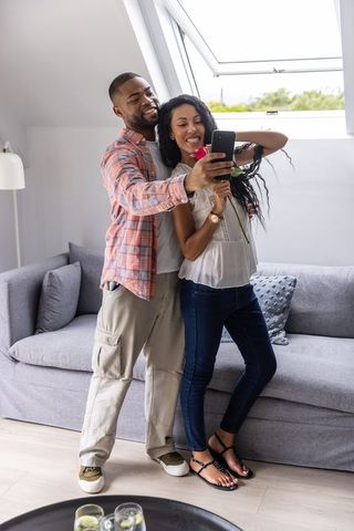 Young couple taking selfie with rose in sunlit modern loft, casual romance moment