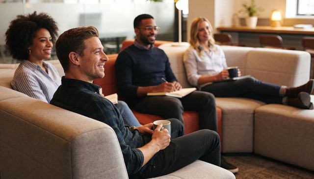 Team relaxing in modern office lounge holding coffee and taking notes for casual coworking