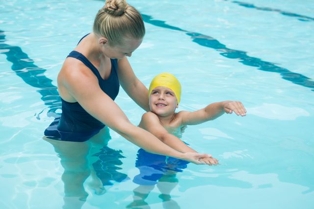 Female swim instructor helping young boy learn swimming in pool. Useful for content related to swimming lessons, aquatic education, child sports training, and pool safety.