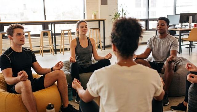 Colleagues meditating together in office lounge practicing mindfulness and breathwork for wellness