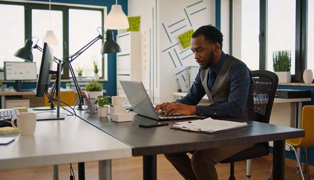African american professional typing on laptop in modern open-plan office, focused