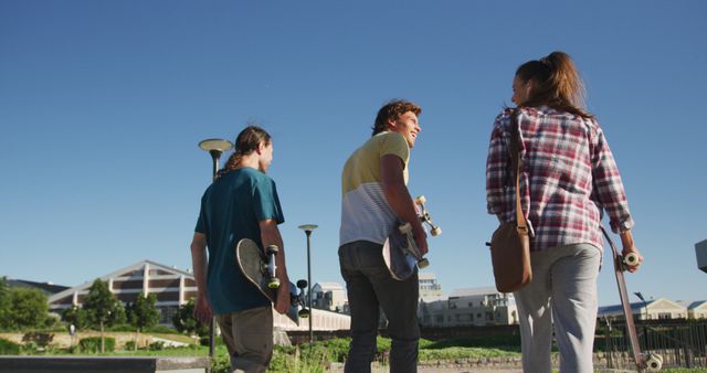 Group of teenagers holding skateboards and smiling while walking outside on a sunny day. Perfect for concepts related to outdoor activities, friendship, youthful fun, and recreational sports.