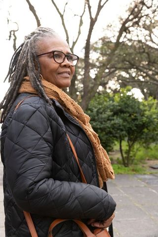 Confident senior african american woman wearing quilted coat and brown scarf in park