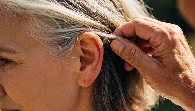 Sunlit hand tucking senior woman's gray hair behind ear closeup of tenderness and care