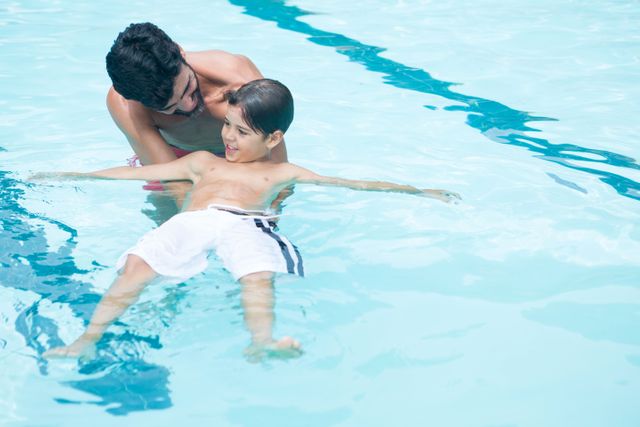 Father teaching his son to swim in a pool, showcasing family bonding and outdoor fun. Ideal for use in advertisements for swimming lessons, family activities, summer camps, and leisure centers.