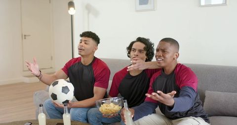 Friends cheering during soccer match on couch with snacks and bottled drinks for game day