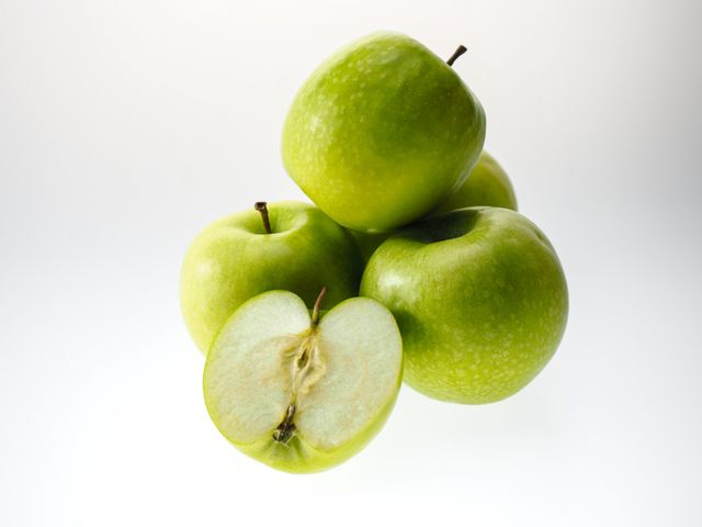Cluster of fresh green apples with one cut in half on a white background. Ideal for use in health food, nutrition, and healthy lifestyle projects. Great for food blogs, restaurant menus, and dietary articles.