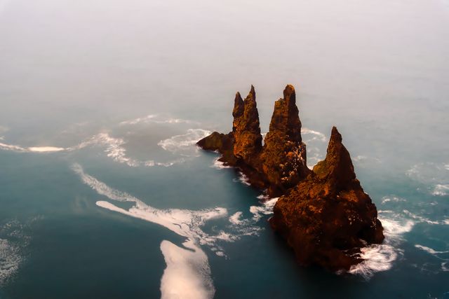 This dramatic rock formation amidst a foggy ocean brings a sense of mystery and awe. Suitable for use in travel blogs, websites promoting nature excursions, magazines focusing on geology, or calming background images for relaxation apps.