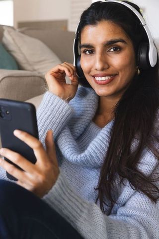 Smiling South Asian Woman Taking Selfie with Headphones and Smartphone at Home