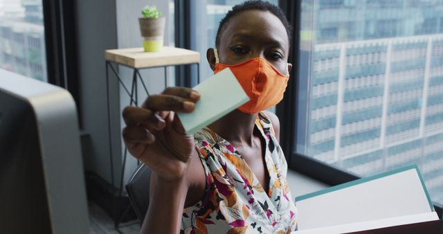 Businesswoman Wearing Face Mask Holding Card in Modern Office - Download Free Stock Images Pikwizard.com