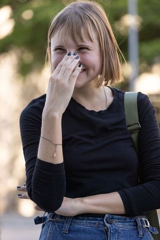 Young woman laughing while covering face with hand in city park wearing black top
