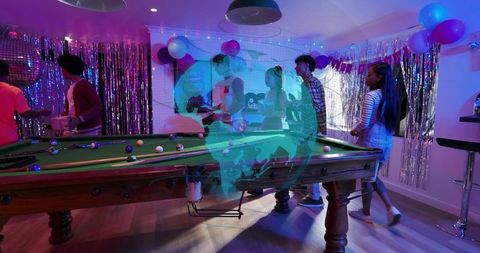 Friends playing pool at neon party with holographic globe projection