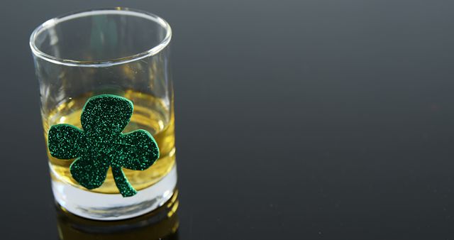 Shot glass containing whiskey with a green glittering shamrock decoration on it. Ideal for St. Patrick's Day marketing, Irish-themed events, party invitations, bar promotions, and festive advertising materials.