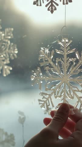 Hands hanging delicate snowflake ornament on frosted window, backlit winter vertical video